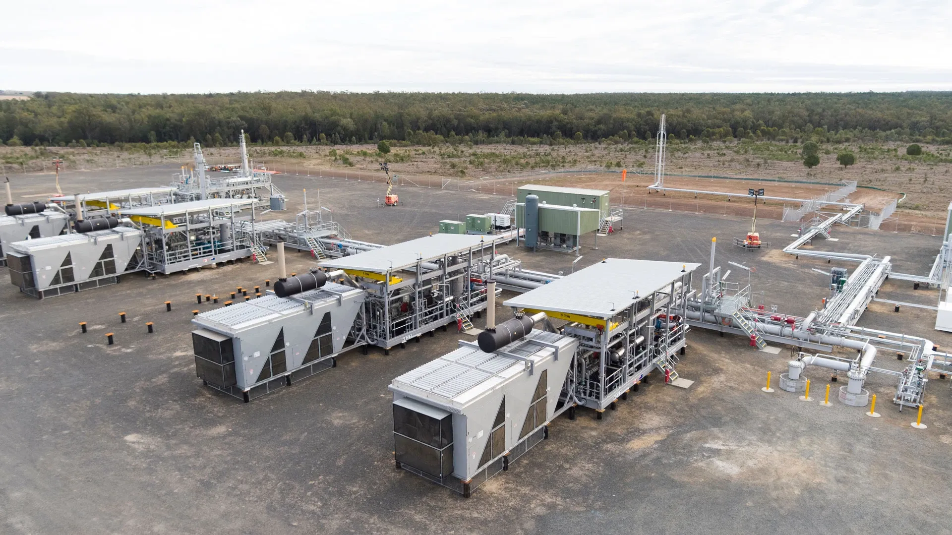 Aerial view of an industrial gas plant with several large metal structures, pipes, and equipment, set on a cleared area surrounded by trees and vegetation.